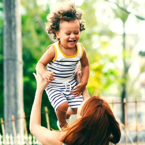 Protecting her car loan with Payment Protection, this woman throws her child in the air while experiencing peace of mind.