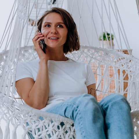 woman in white shirt and blue jeans sitting in chair while using phone