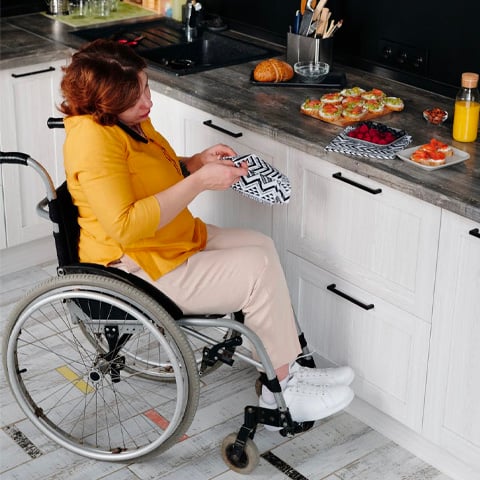 woman in yellow t shirt sitting in wheel chair preparing food in kitchen