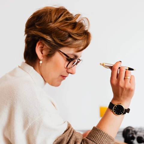 Woman in white sweater holding pen looking down at desk