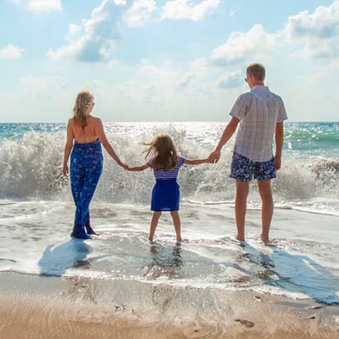 man, woman and child holding hands on the beach